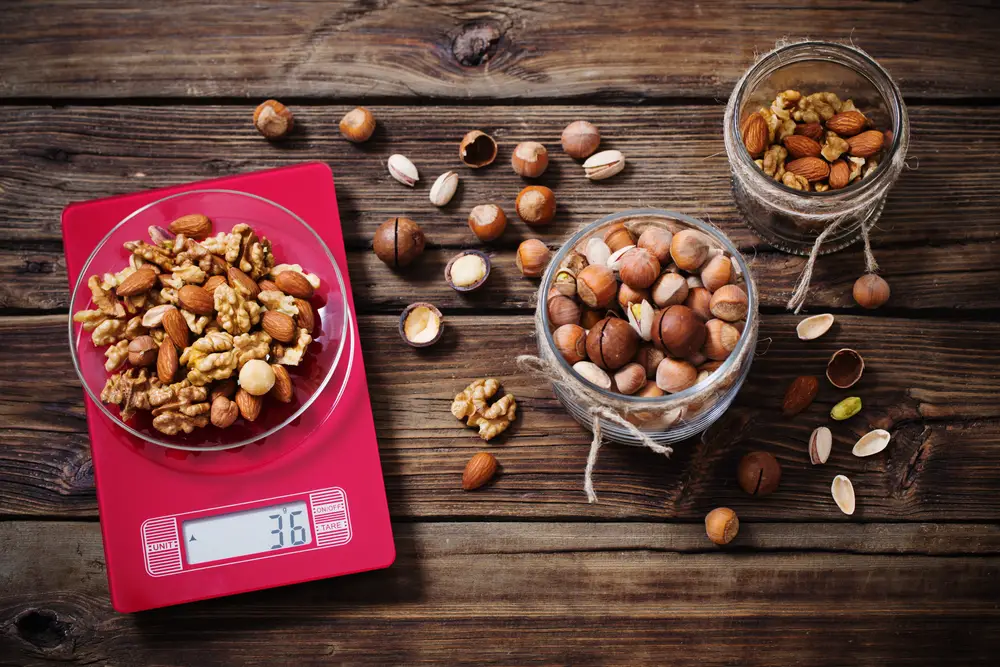 a mix of different nuts in a bowl and jar on a wooden table