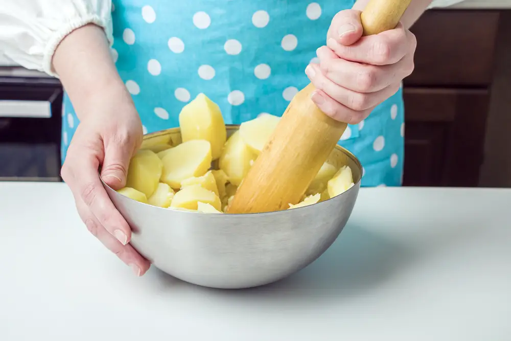 Woman smashing boiled food in the bowl using a wooden tool