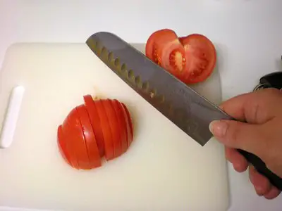 a tomato being sliced on a chopping board